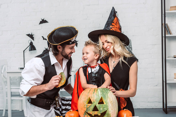retrato de pais e filho em trajes de Halloween à mesa com abóboras em casa
 - Foto, Imagem