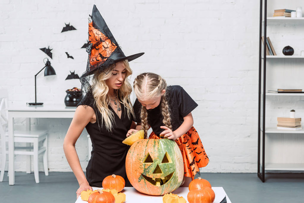 portrait of mother and little daughter in witches costumes at coffee table with pumpkins at home - Valokuva, kuva