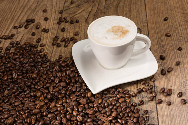 kopje Cappuccino en koffie bonen op houten tafel - Foto, afbeelding