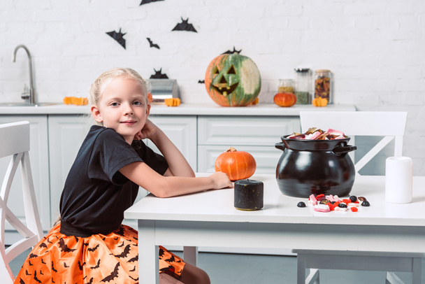 side view of cute kid sitting at table with halloween treats in black pot at home - Φωτογραφία, εικόνα