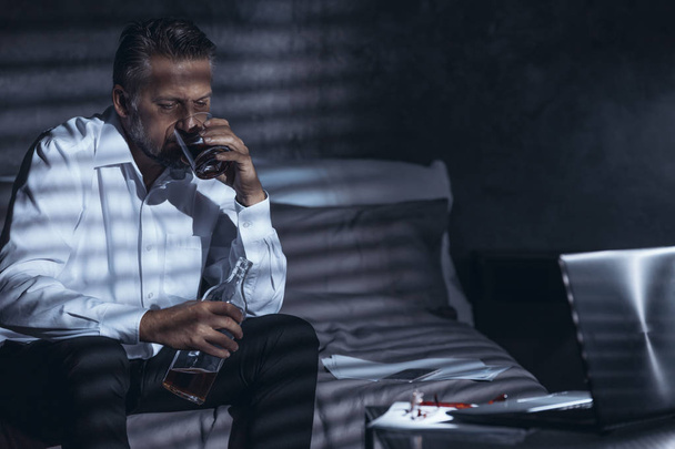 Lonely workaholic with alcohol problem sitting alone in the dark - 写真・画像