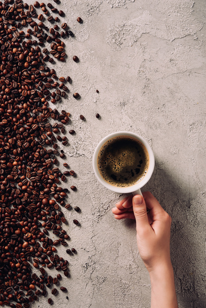 こぼれたコーヒー豆とコンクリートの表面にコーヒーのカップを保持している女性のクロップ撮影 - 写真・画像