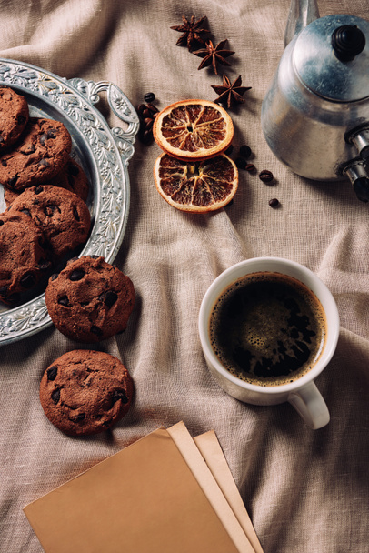 κάτοψη του καφέ με το βιβλίο και μπισκότα τσιπ σοκολάτας σε μπεζ ύφασμα - Φωτογραφία, εικόνα
