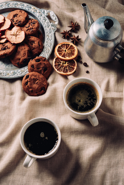 top view of cups of coffee with chocolate chip cookies and vintage metal pot on beige cloth - Фото, зображення