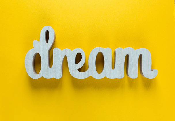 dream - inspirierendes Wort mit Holzbuchstaben auf leuchtend gelbem Hintergrund, Typografie für Plakate, T-Shirts oder Karten. flache Lage, Kopierraum  - Foto, Bild
