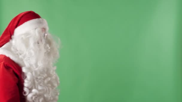 Santa Claus belép a test-val egy zsák, keresse meg a kamera, és intett a kezével, üdvözlő mozdulattal zöld chroma-key a háttérben. - Felvétel, videó