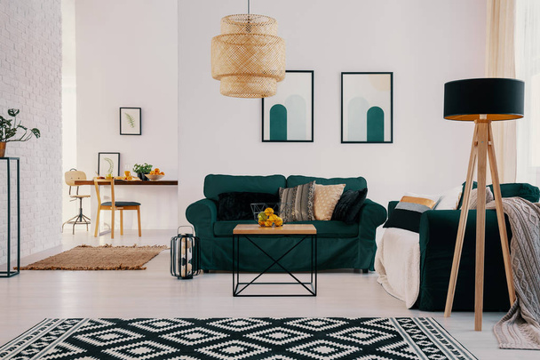 Patterned carpet and lamp in bright open space interior with posters above green settee. Real photo - Foto, afbeelding
