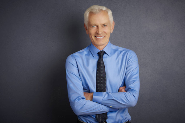 smiling mature man wearing shirt and tie standing with folded arms at dark grey background.  - Fotoğraf, Görsel