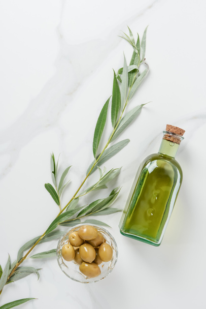 pohled shora na láhev olivového oleje a olivy v misce na mramorový stůl - Fotografie, Obrázek