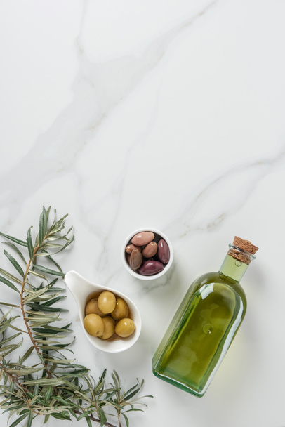 top view of olive oil and yummy olives in bowls on marble table  - Fotó, kép