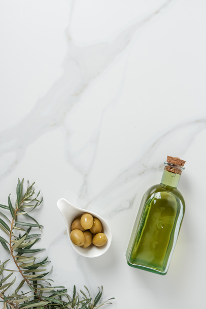 top view of bottle of olive oil and olives in bowl on marble surface - Фото, изображение