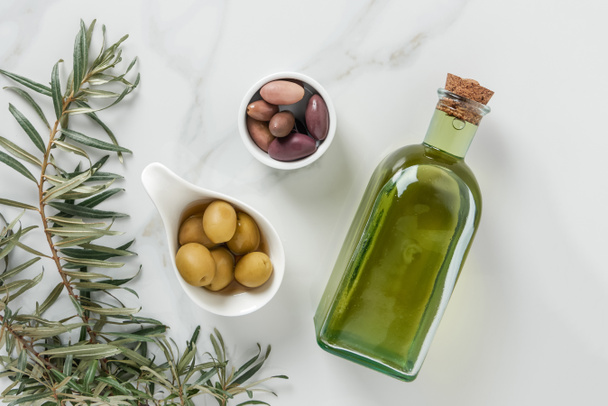 top view of olive oil and yummy olives in bowls on marble surface - Photo, Image
