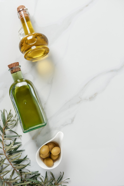 top view of olive oil in glass bottles and olives on marble tabletop - Fotografie, Obrázek