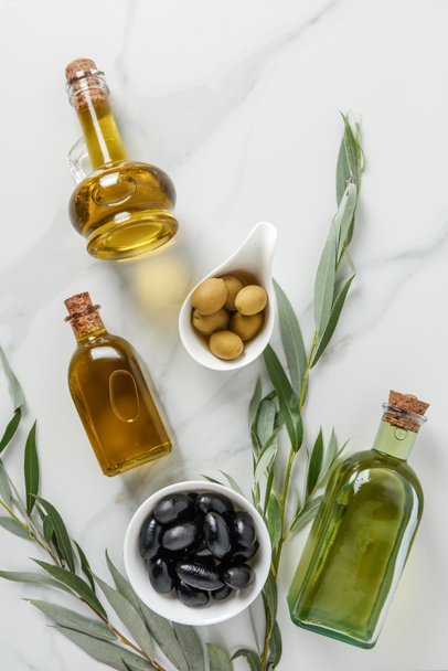 top view of olive oil in glass bottles and tasty olives on marble table - Фото, изображение