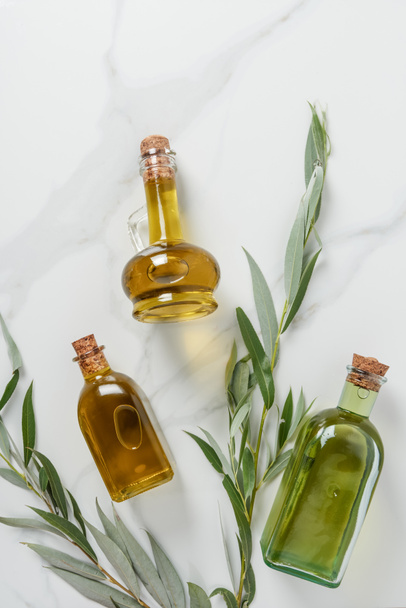 top view of bottles of three bottles of olive oil and twigs on marble table  - Фото, зображення