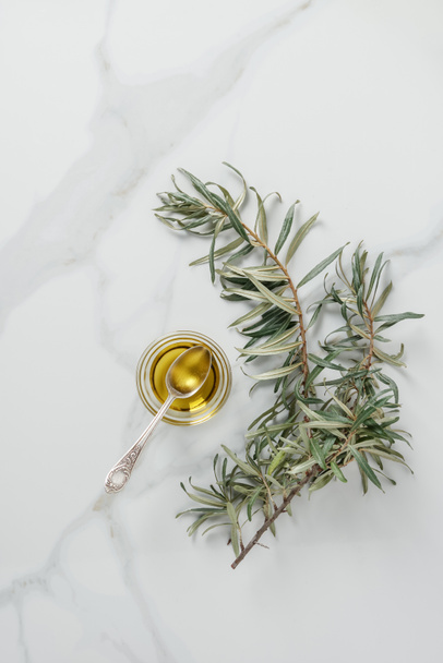 top view of olive oil and spoon in glass on marble table - Foto, afbeelding
