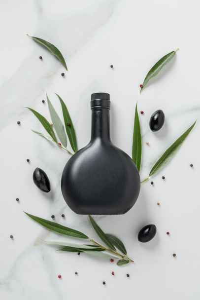 top view of black bottle of olive oil and olives on marble table - Фото, изображение