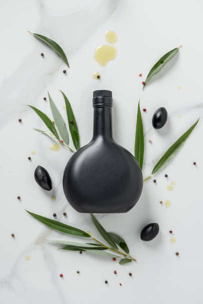 elevated view of black bottle of olive oil and olives on marble table - Foto, Bild