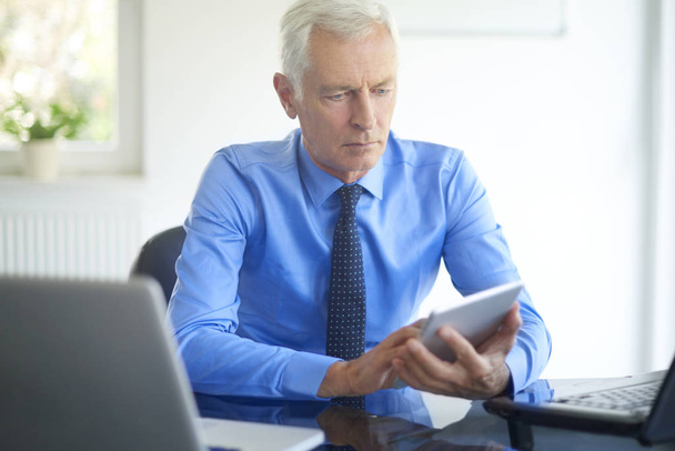 handsome businessman using digital tablet in office. Senior professional man wearing shirt and tie and working on new financial strategy.  - 写真・画像