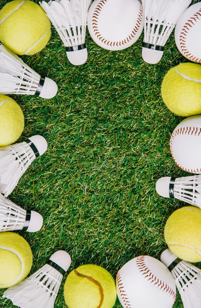 top view of arrangement of badminton shuttlecocks, tennis and baseball balls on green lawn - Фото, изображение