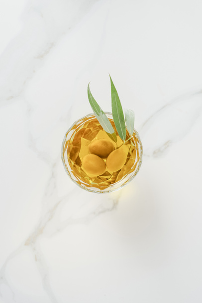 вид на оливковую ветку с оливками в стекле на мраморном столе
 - Фото, изображение