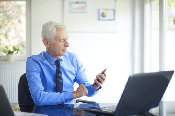 Portrait of senior financial consultant businessman sitting at office and text messaging.   - Foto, Bild
