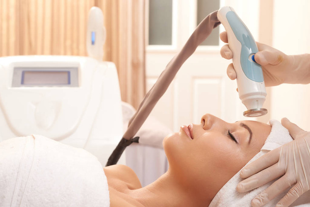Young relaxed woman having electric device over face during revitalizing beauty procedure - Photo, Image
