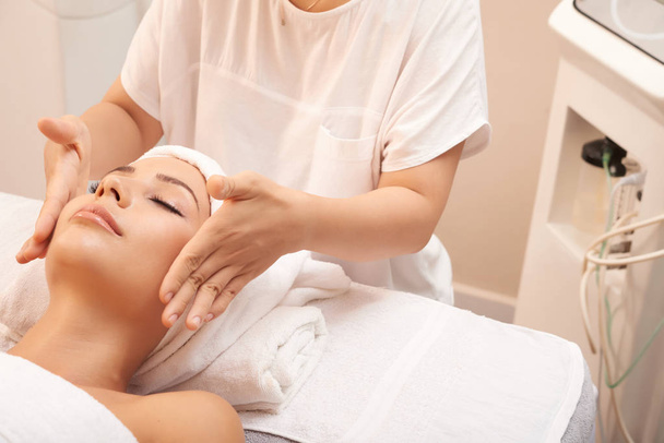 Young beauty specialist touching cheeks of client to calm skin down after skincare procedure - Foto, imagen