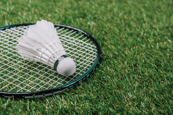 close up view of white shuttlecock and badminton racket lying on green grass - Фото, изображение