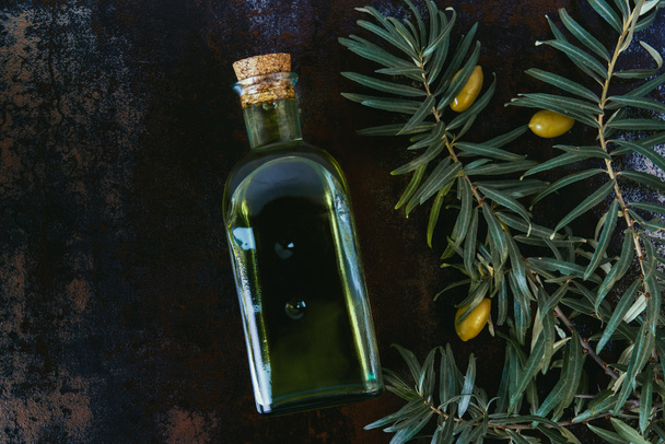 top view of bottle of tasty olive oil, twigs and olives on shabby surface - Photo, Image
