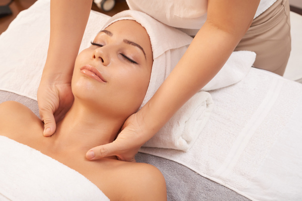 Jovem mulher deitada em toalhas suaves no salão de spa e desfrutando de massagem relaxante de seu pescoço
 - Foto, Imagem