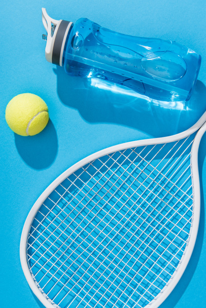 vista de cerca de la botella de agua deportiva y el equipo de tenis en el fondo azul
 - Foto, Imagen