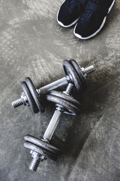 top view of adjustable dumbbells with sneakers on concrete surface - Foto, imagen