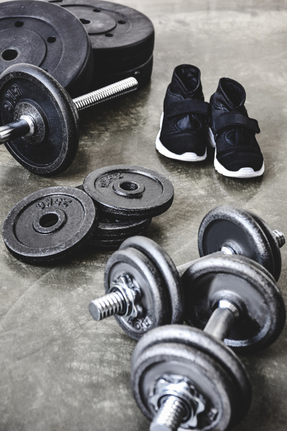 dumbbells and barbell with weight plates and sneakers on concrete floor - Фото, изображение