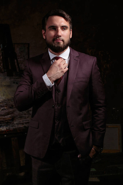 A confident elegant handsome young man standing in front of a black background in a studio wearing a nice suit. businessman - Fotó, kép