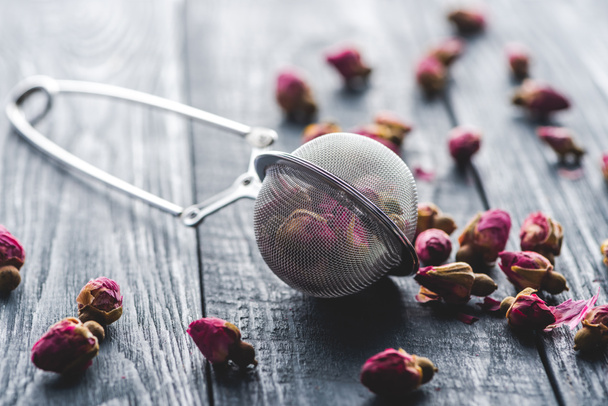 dried rose buds tea and tea strainer on wooden table - Photo, Image