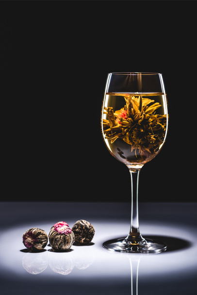 ποτήρι κινεζική ανθοφορία τσάι με τσάι μπάλες στο τραπέζι που απομονώνονται σε μαύρο - Φωτογραφία, εικόνα