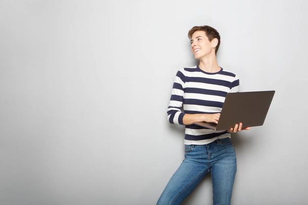 Retrato de jovem mulher alegre segurando computador portátil contra fundo cinza
 - Foto, Imagem