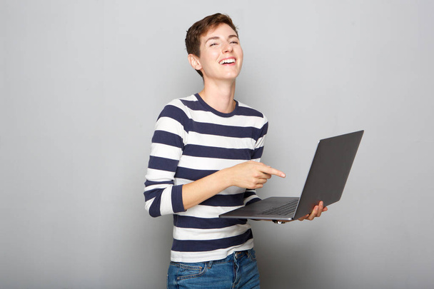 Porträt einer glücklichen jungen Frau, die ihren Laptop hält und auf den Bildschirm zeigt - Foto, Bild
