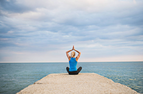Visão traseira de uma jovem mulher esportiva fazendo exercício de ioga pelo oceano fora
. - Foto, Imagem
