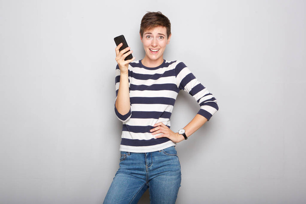 Portrait of young woman holding mobile phone with surprised expression - Photo, Image