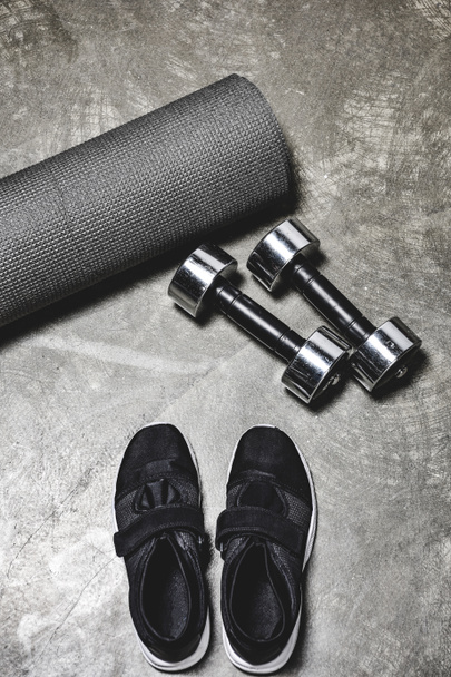 high angle view of view of sporting shoes with yoga mat and dumbbells lying on concrete surface - Fotografie, Obrázek