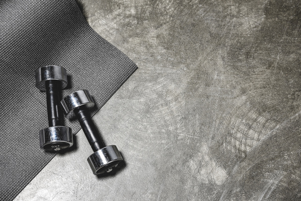 top view of yoga mat and dumbbells lying on concrete surface - Foto, Bild