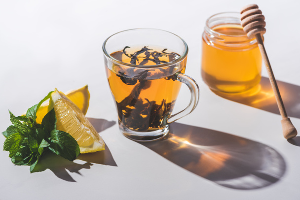 healthy black tea with honey, lemon and mint on white tabletop - Foto, afbeelding