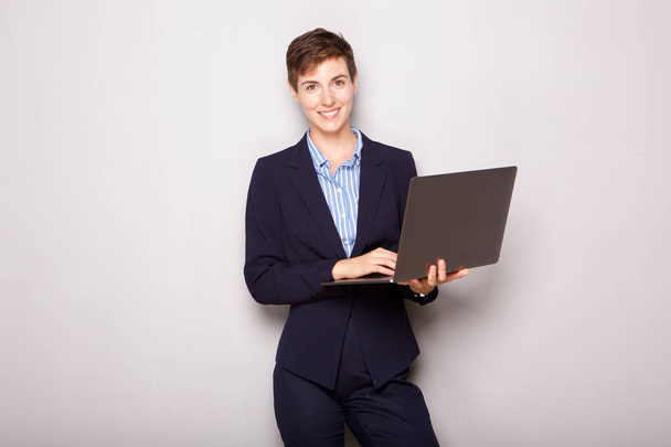Portrait of young business woman holding laptop computer by white background - Photo, Image