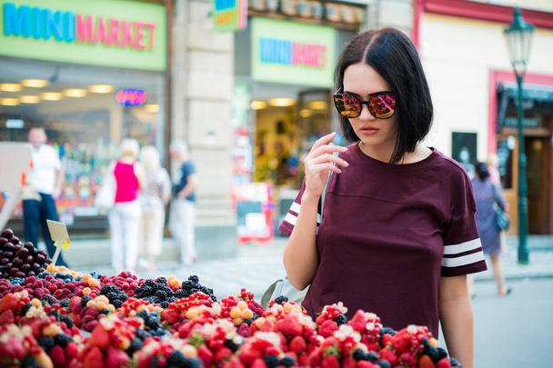 Concentrated young woman buying berries on a street market. - Photo, image