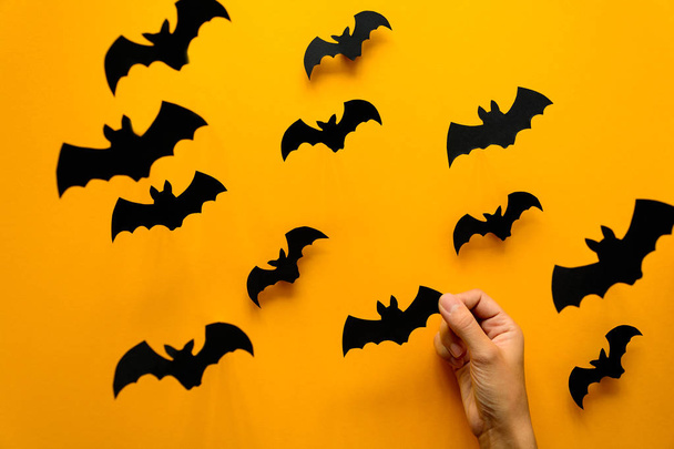 Woman's hand holding bat and black paper bats flying on yellow background. Halloween concept. Paper cut - Foto, imagen