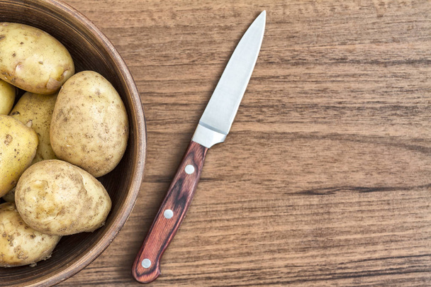 Raw potatoes in a clay bowl, close-up. - Фото, изображение