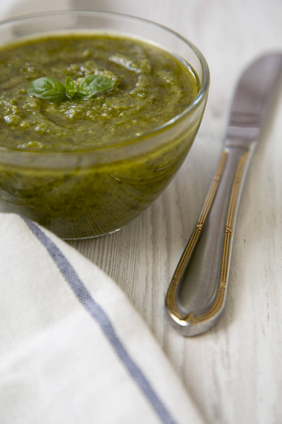 Bowl of freshly made basil pesto and knife on white wooden table, side view. Close-up.  - Fotó, kép