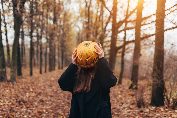 A terrible creature in the autumn forest in the evening. Happy Halloween. Pumpkin head. Man with a pumpkin on his head and a black cloak - 写真・画像